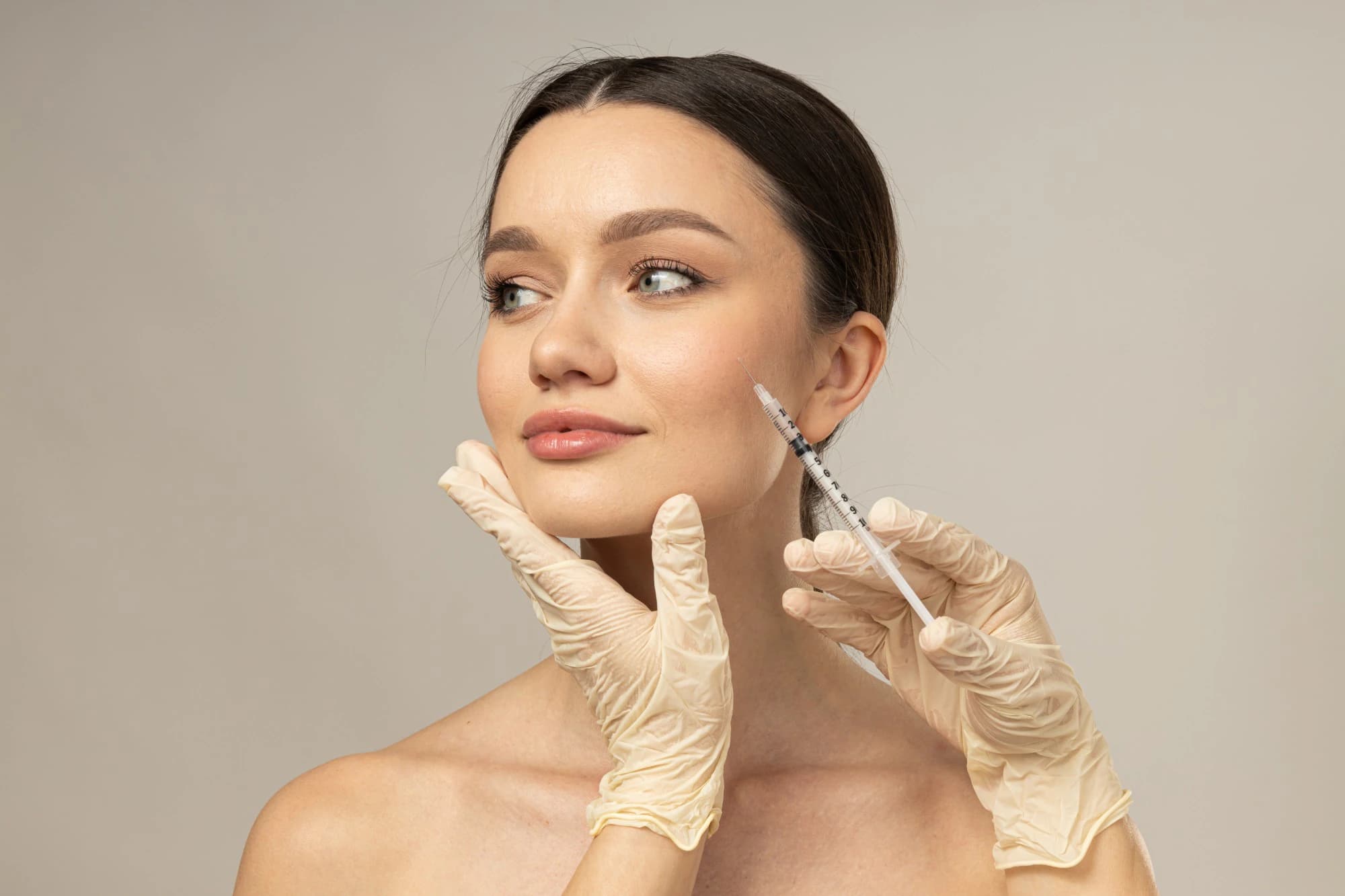 A woman looking aside while a gloved provider holds a syringe near her cheek, illustrating Botox® before and after care