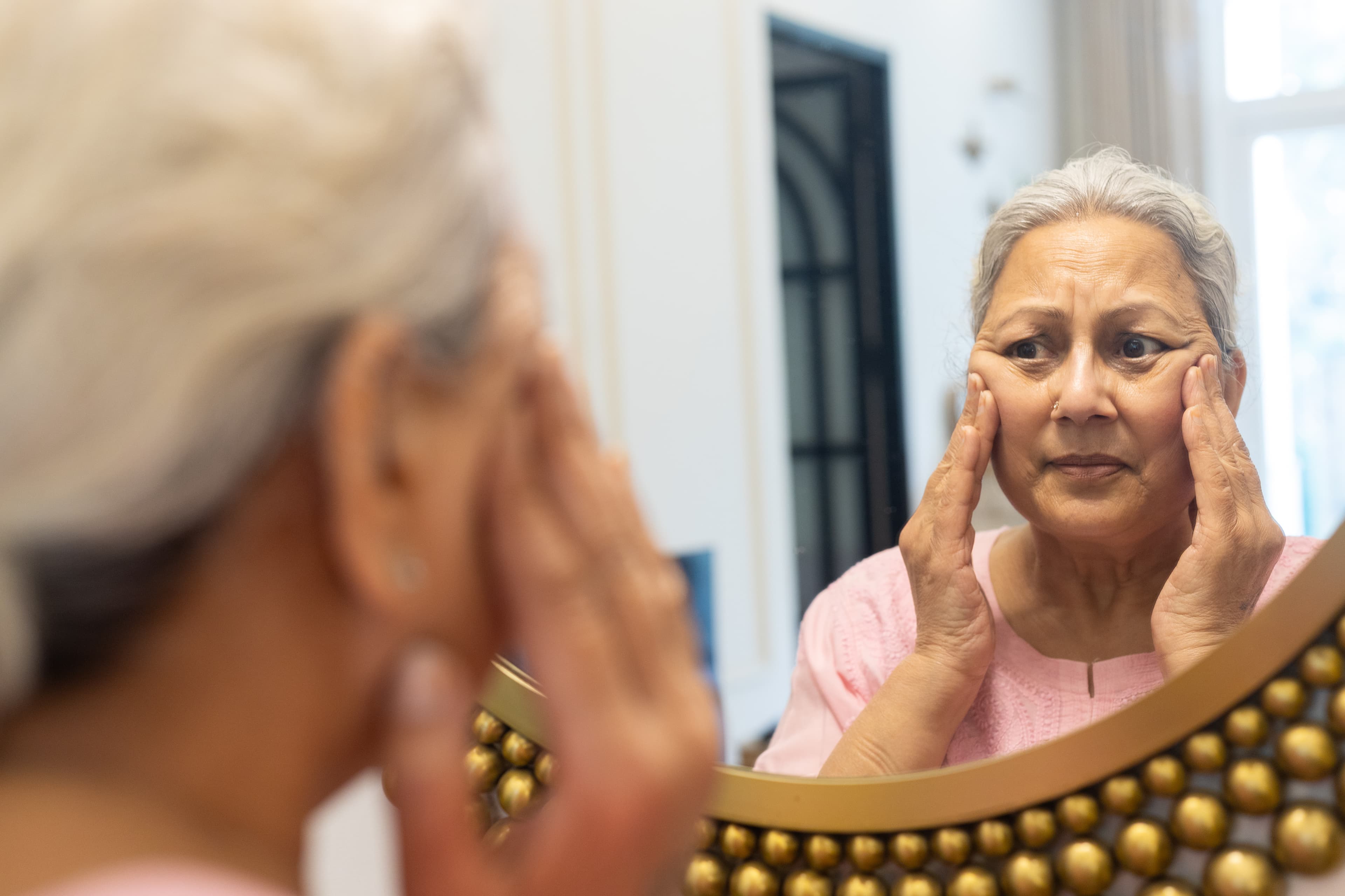 A woman examining the fine lines around her eyes in a mirror