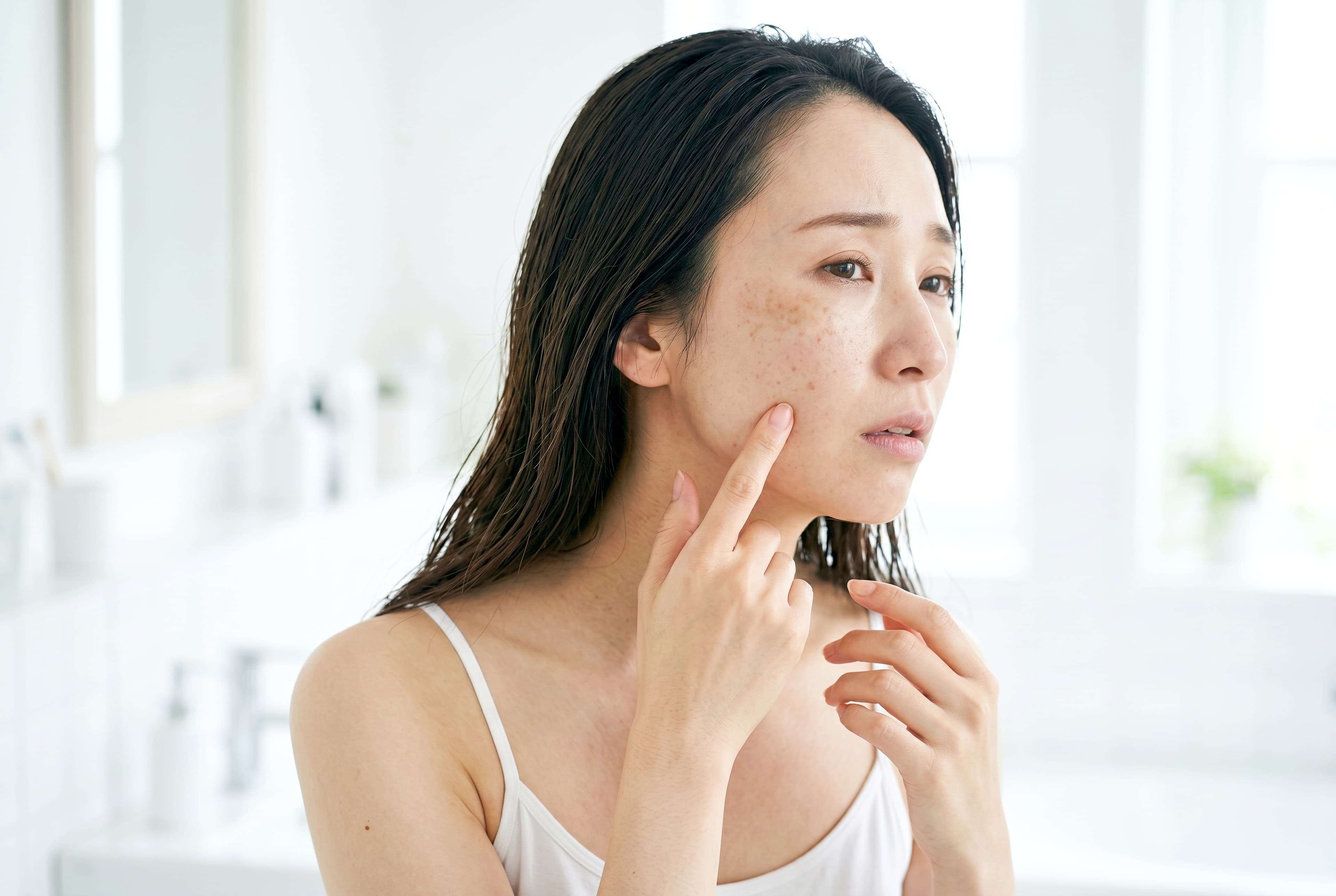 A woman examining areas of pigmentation on her cheek