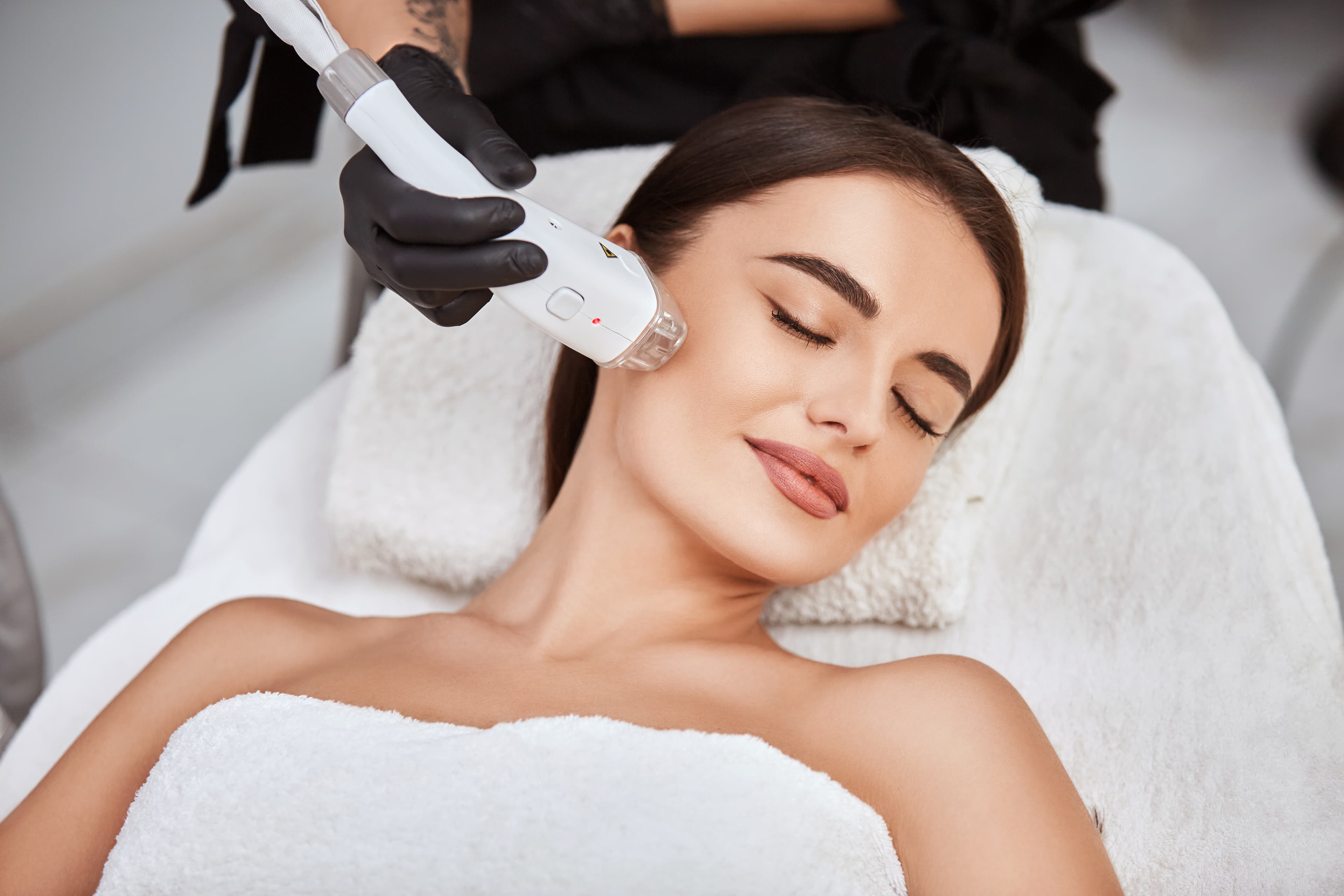 A provider using a handheld laser device on a client's cheek during a treatment