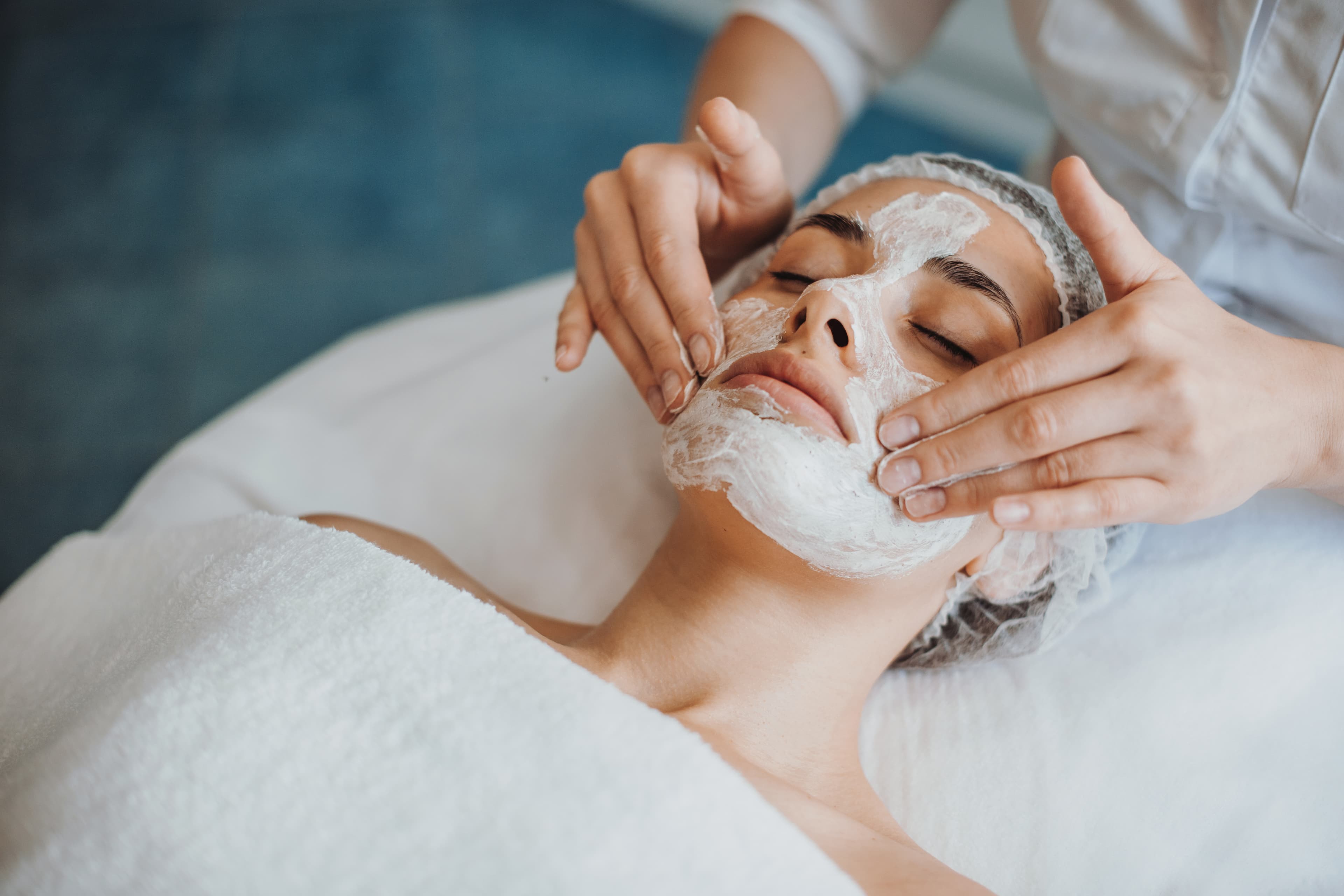 An esthetician applying a cleansing mask to a client's face during a spa facial
