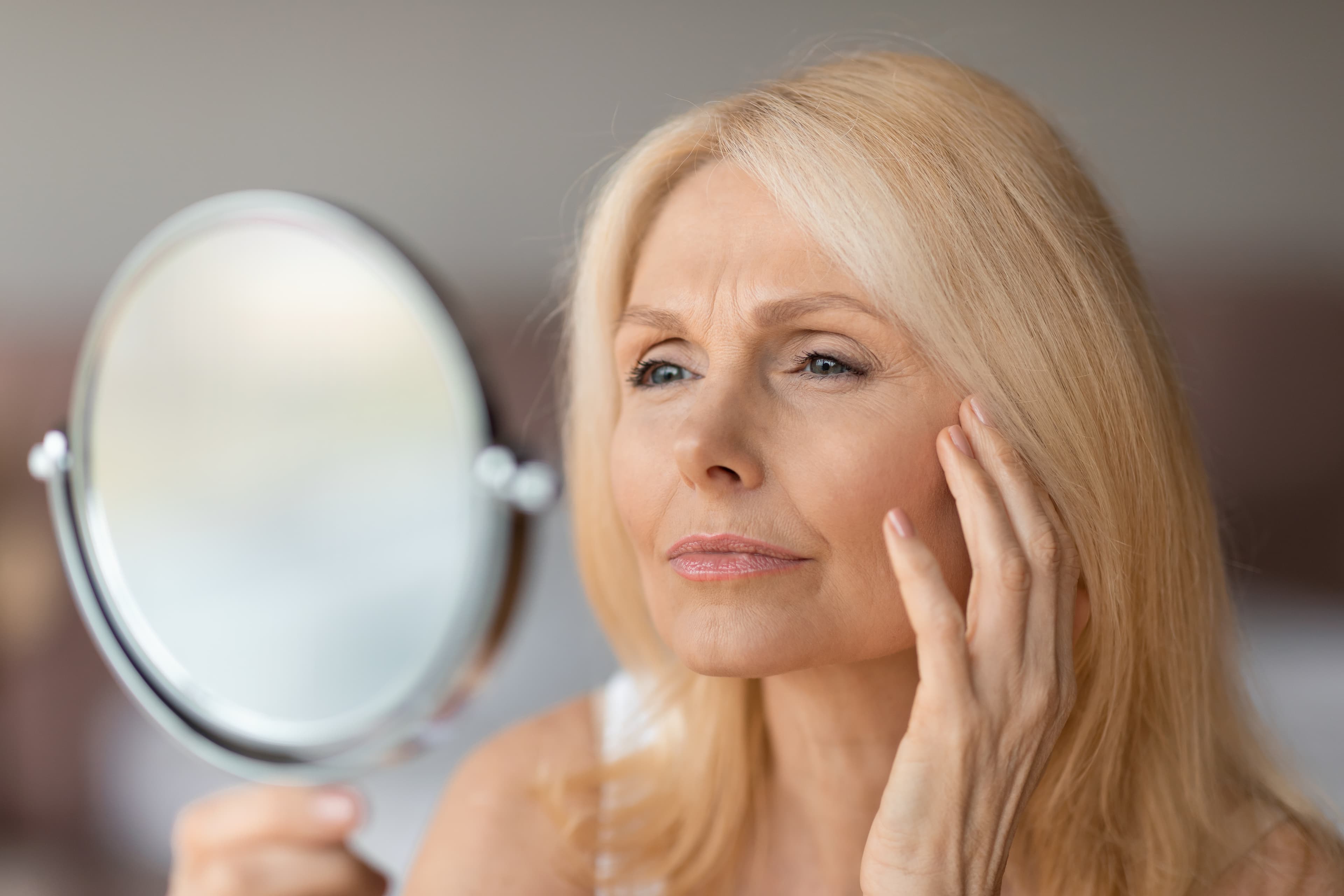 A mature woman examining wrinkles in a hand mirror