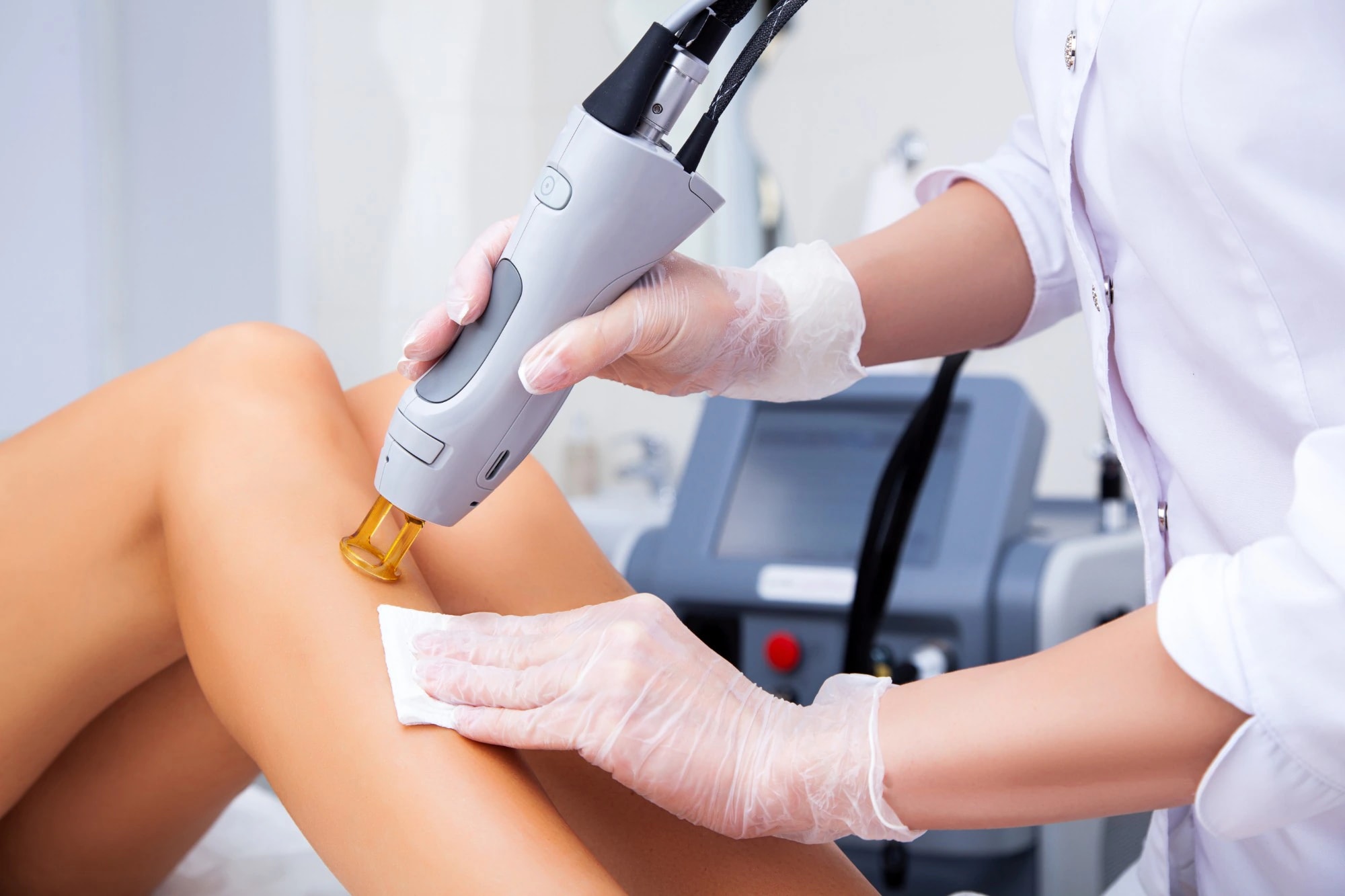 A provider in gloves using a laser hair removal handpiece on a client's lower leg