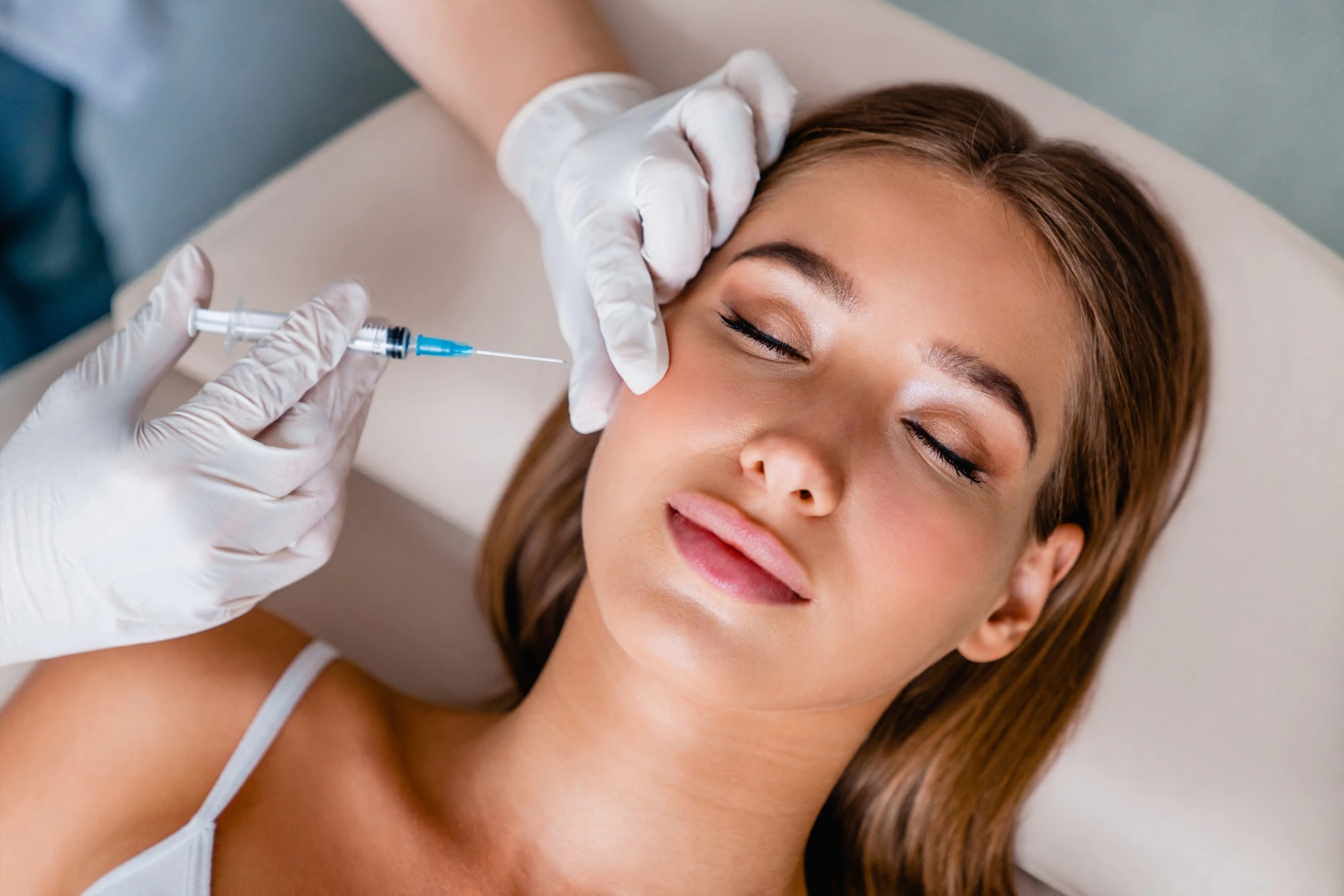 A woman lying back with her eyes closed while a gloved provider holds a syringe near her cheek during a Botox® treatment